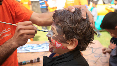 a side view of a guy painting a toddler's face