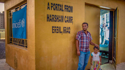 A man and his daughter standing at a yellow wall with writings on it