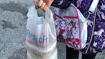 A female carrying a plastic bag with "PlasticFri" writing on it