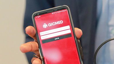 Someone's hand holding the phone with GICMED login page on screen