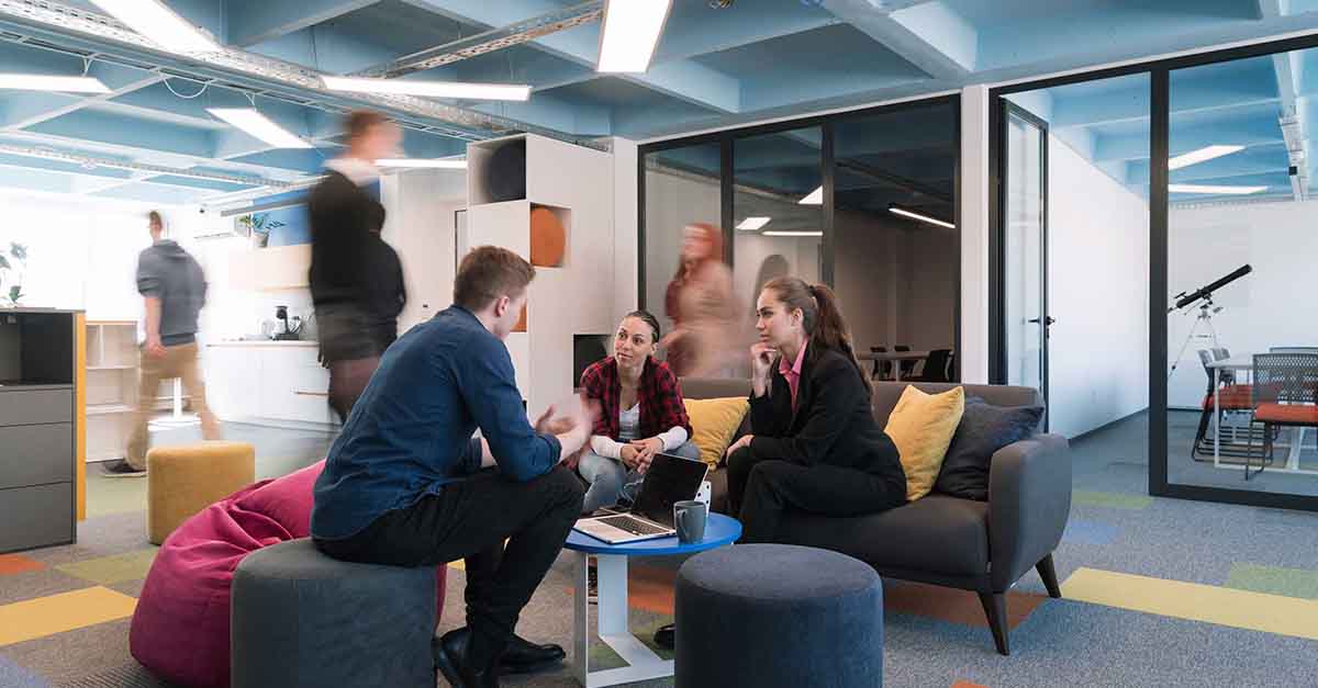 Foto: Junge Kollegen konferieren in einer modernen Bürowelt auf Sesseln