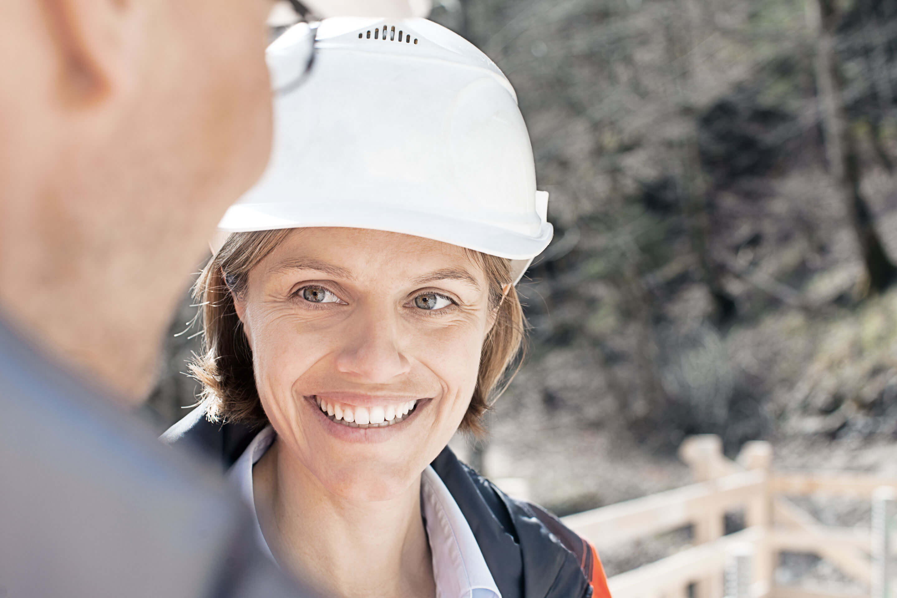 Bild: STRABAG Mitarbeiterin mit weissem Sicherheitshelm auf einer Baustelle.