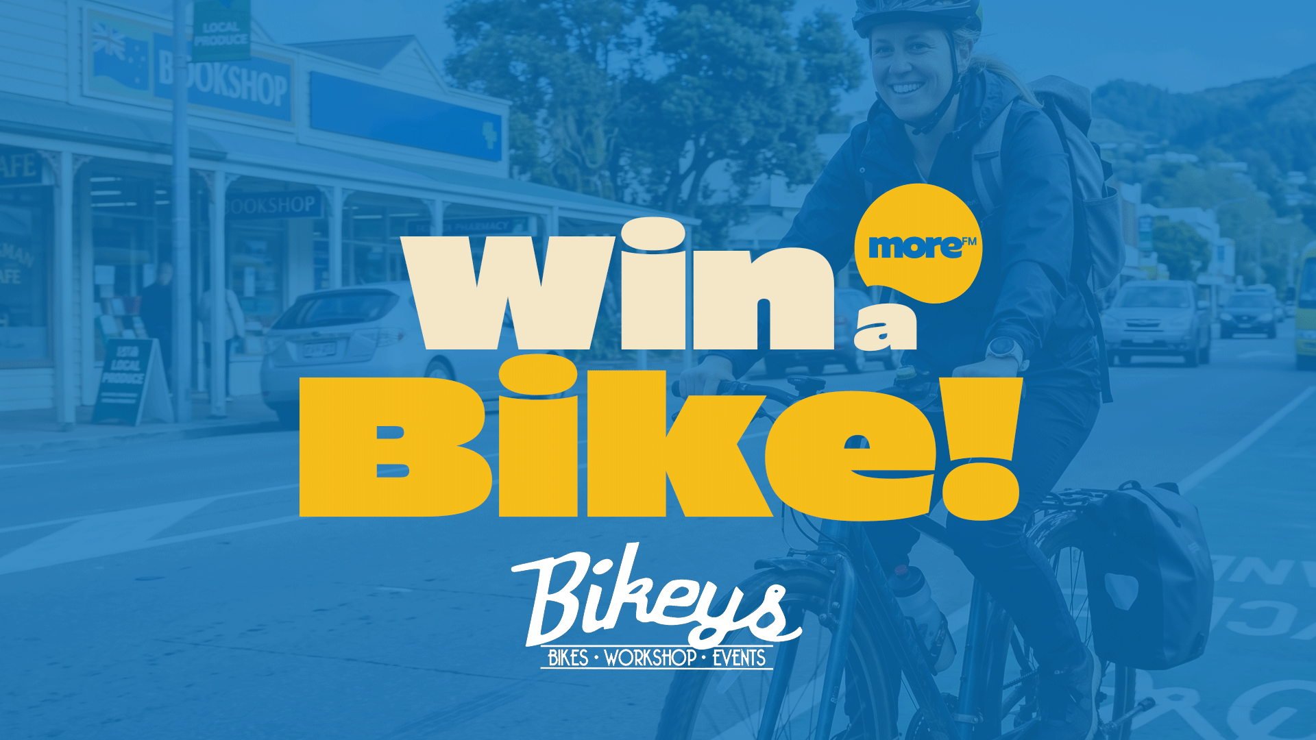 A smiling woman in a helmet rides a bike on a street with cars and buildings, overlaid with large text "Win a Bike!" and "Bikeys" branding, plus a "more™" logo.