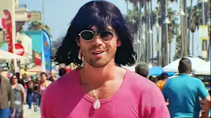Kiwi-born actor KJ Apa walking Venice Beach boardwalk as his TikTok alter ego Mr Fantasy - dressed in a pink shirt, shell pendant necklace, oval sunglasses and a black bob wig with a fringe.
