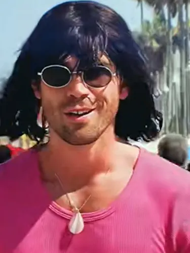 Kiwi-born actor KJ Apa walking Venice Beach boardwalk as his TikTok alter ego Mr Fantasy - dressed in a pink shirt, shell pendant necklace, oval sunglasses and a black bob wig with a fringe.