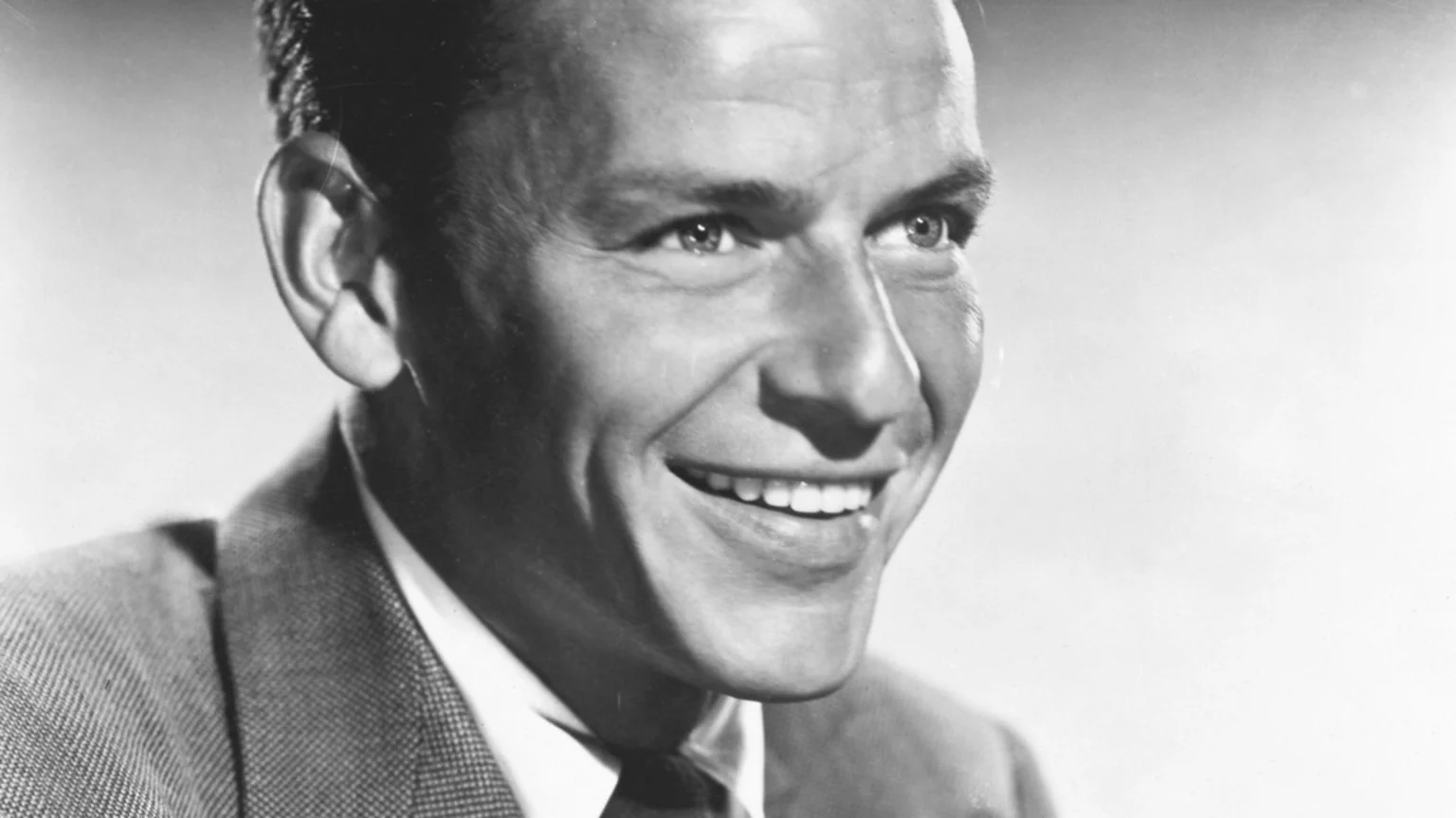 Close-up black and white portrait of Frank Sinatra smiling, wearing a suit and tie.