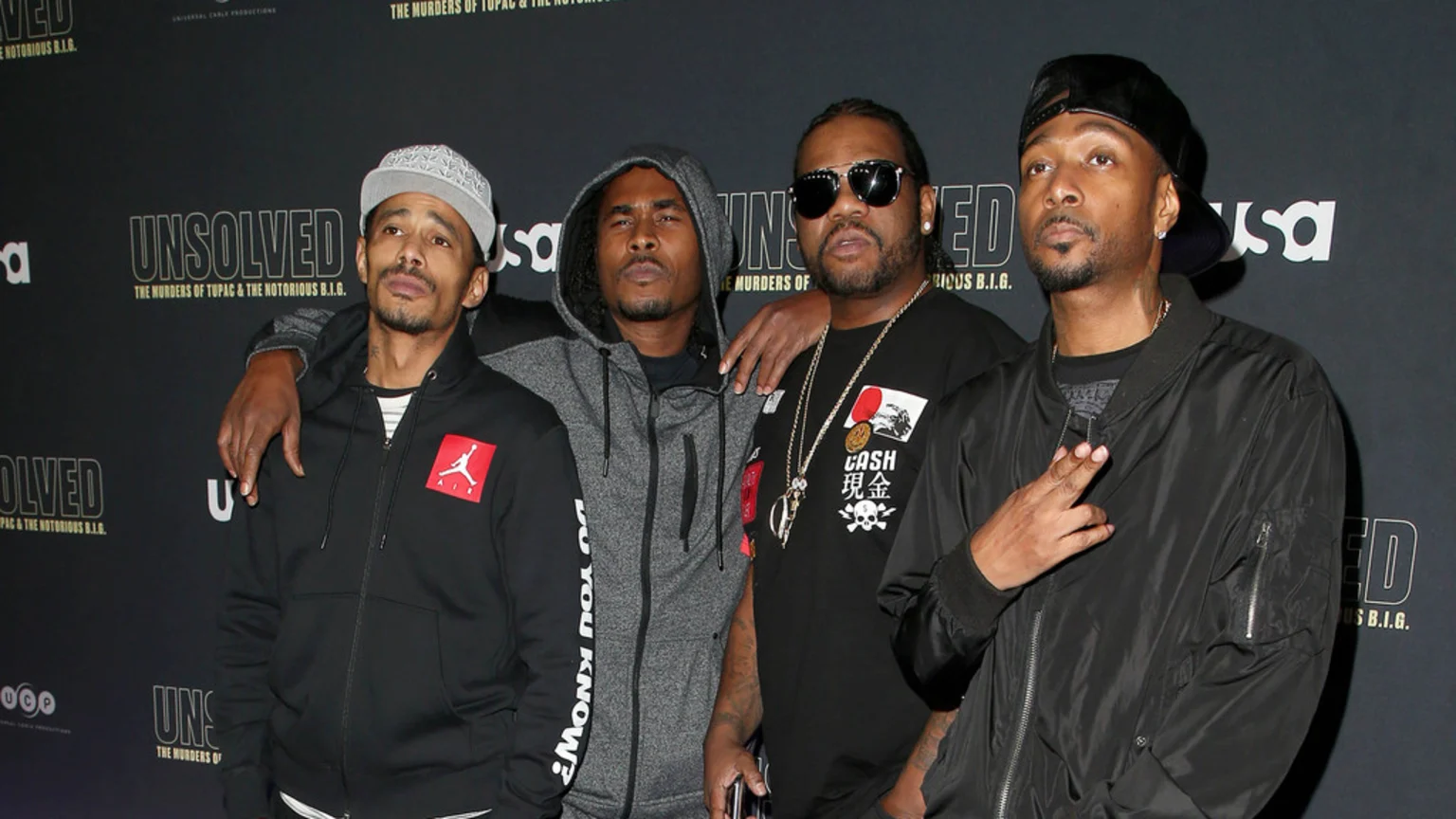 Four men stand together, one in a grey cap, one in a grey hoodie, one in sunglasses and a black tee, and one in a black bomber jacket, against a dark "UNSOLVED" backdrop.
