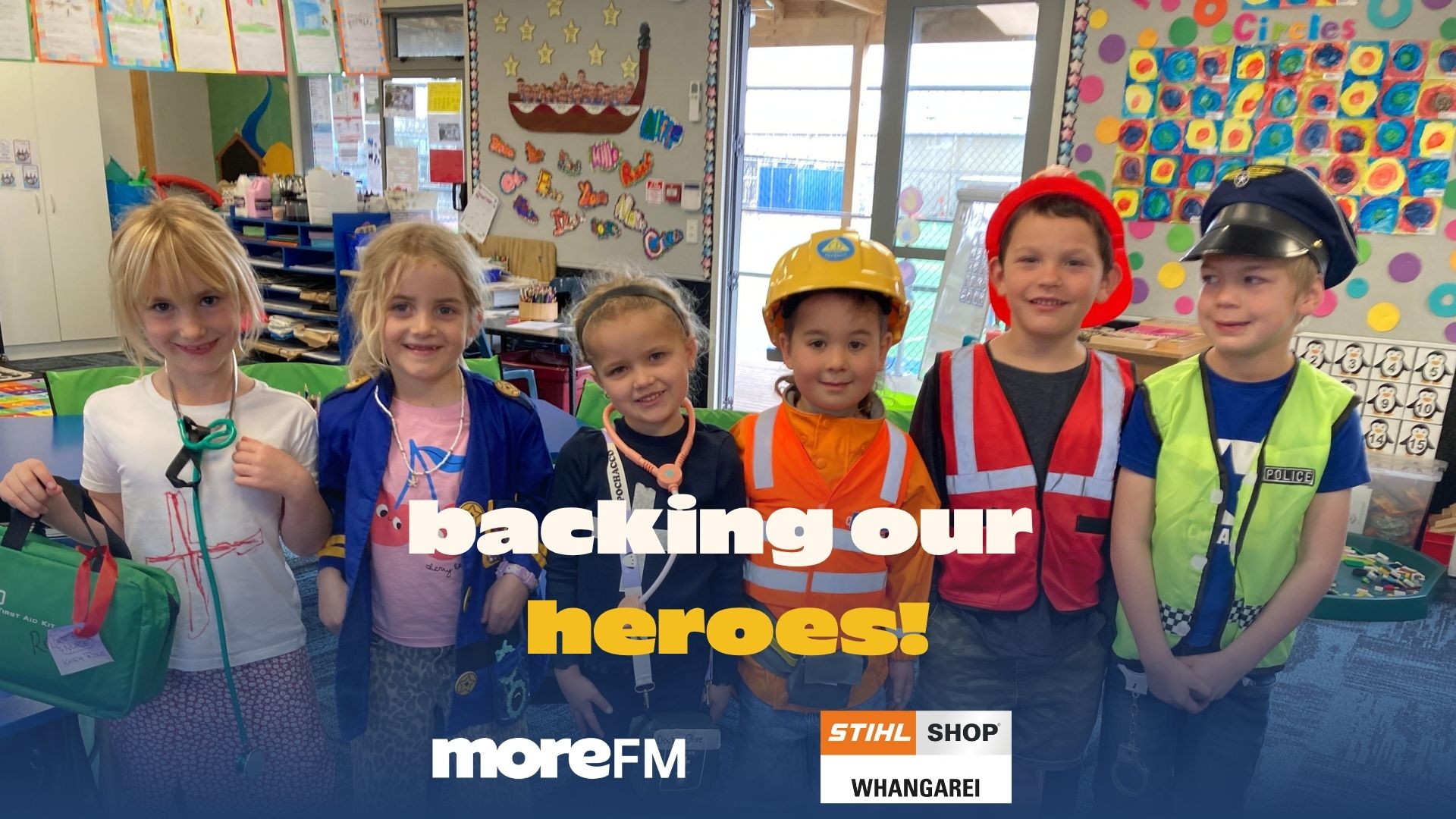 Six smiling children are dressed as community heroes including medics, a construction worker, firefighter, and police officer, in a bright classroom.
