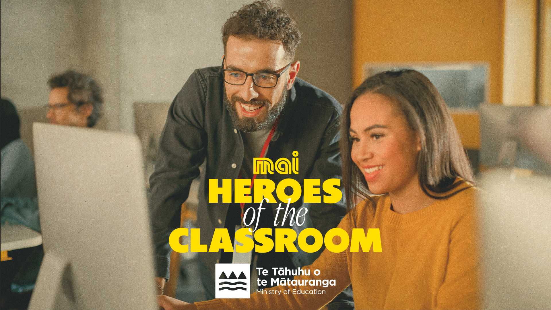 A smiling man and woman look at a computer screen together, with overlay text "mai HEROES of the CLASSROOM" and the Ministry of Education logo and name.