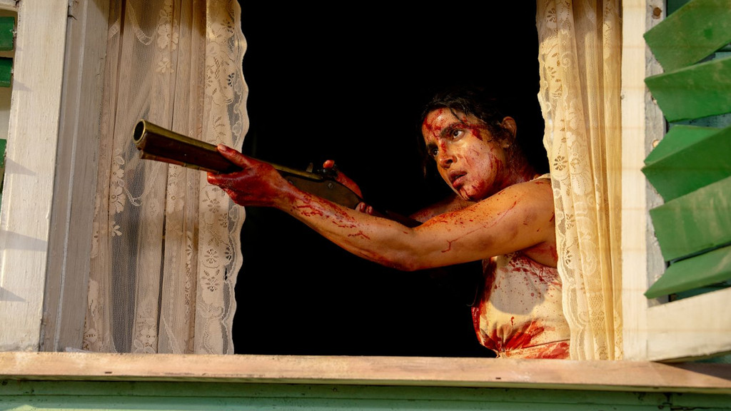 A woman, covered in blood, aims a rifle out of a window with intense focus.