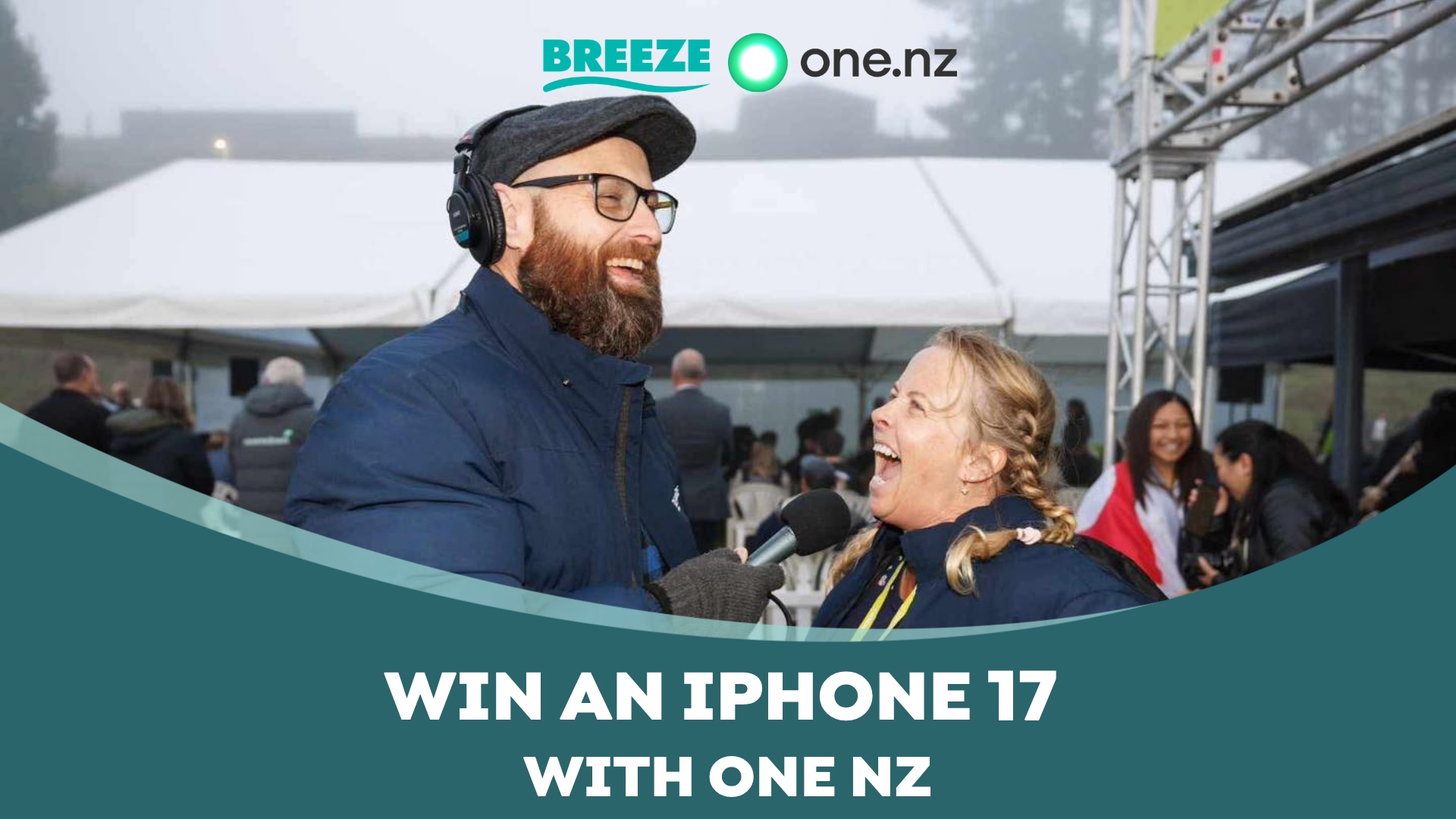 A man with a beard and headphones holds a microphone to a laughing woman at an outdoor event, with "BREEZE one.nz" and "WIN AN IPHONE 17 WITH ONE NZ" text overlays.