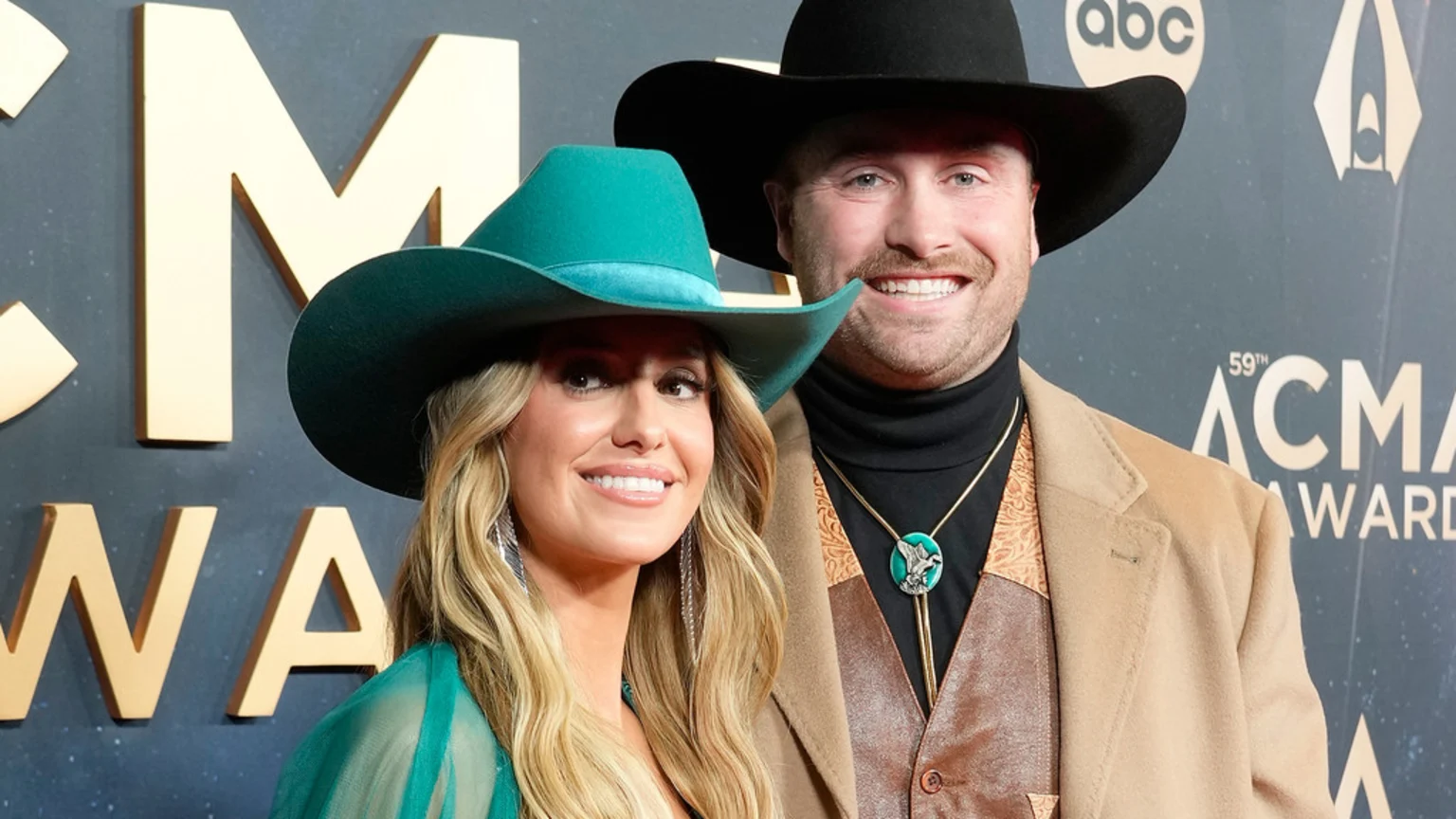 Lainey Wilson in a teal cowboy hat and Devlin 'Duck' Hodges in a black cowboy hat smile at the 59th ACM Awards.