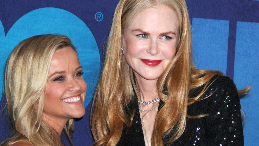 Actresses Reese Witherspoon, smiling on the left, and Nicole Kidman, with red lipstick and a sequined top on the right, pose against a blue background.