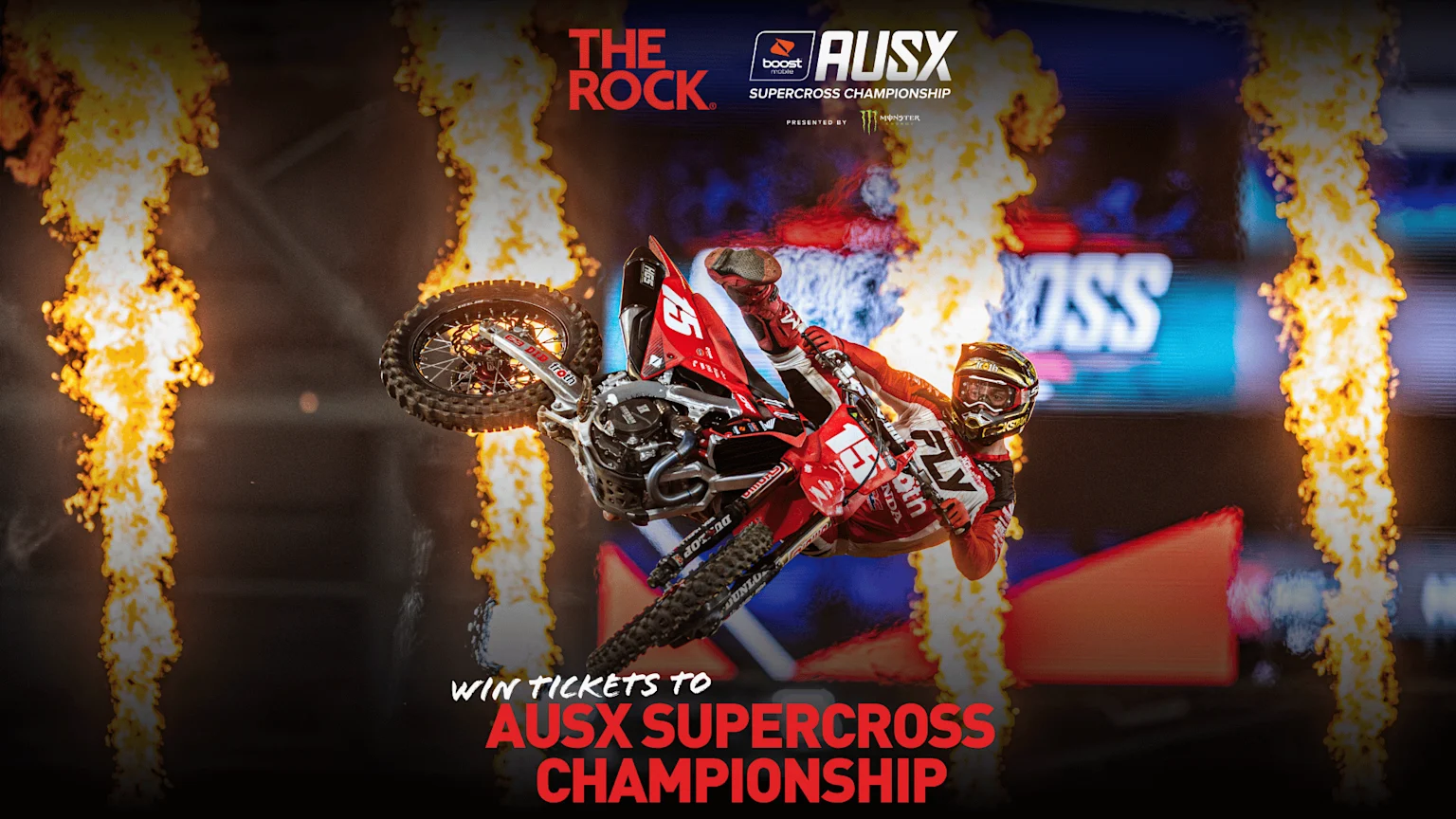 A motocross rider on a red dirt bike performs an aerial trick, surrounded by flames, with "AUSX SUPERCROSS CHAMPIONSHIP" logos at the top and "WIN TICKETS" text at the bottom.