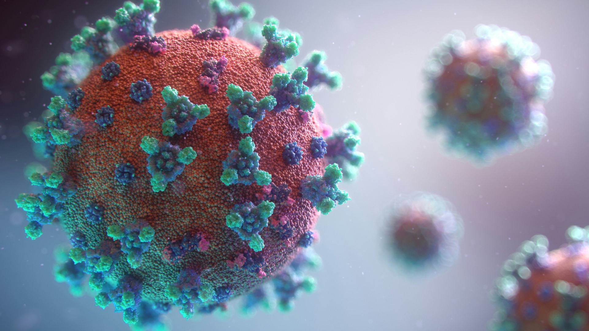 A detailed illustration of a red-orange COVID-19 virus particle with numerous green and purple spike proteins, with several other blurred virus particles in the background.