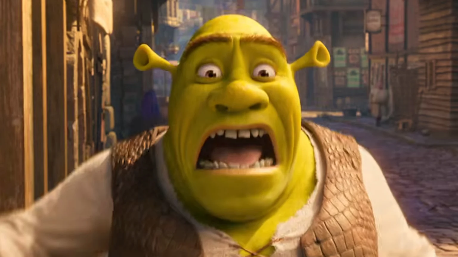 A close-up of Shrek looking shocked, with wide eyes and an open mouth showing teeth and tongue, wearing a brown vest over a white tunic, in a blurry medieval street.