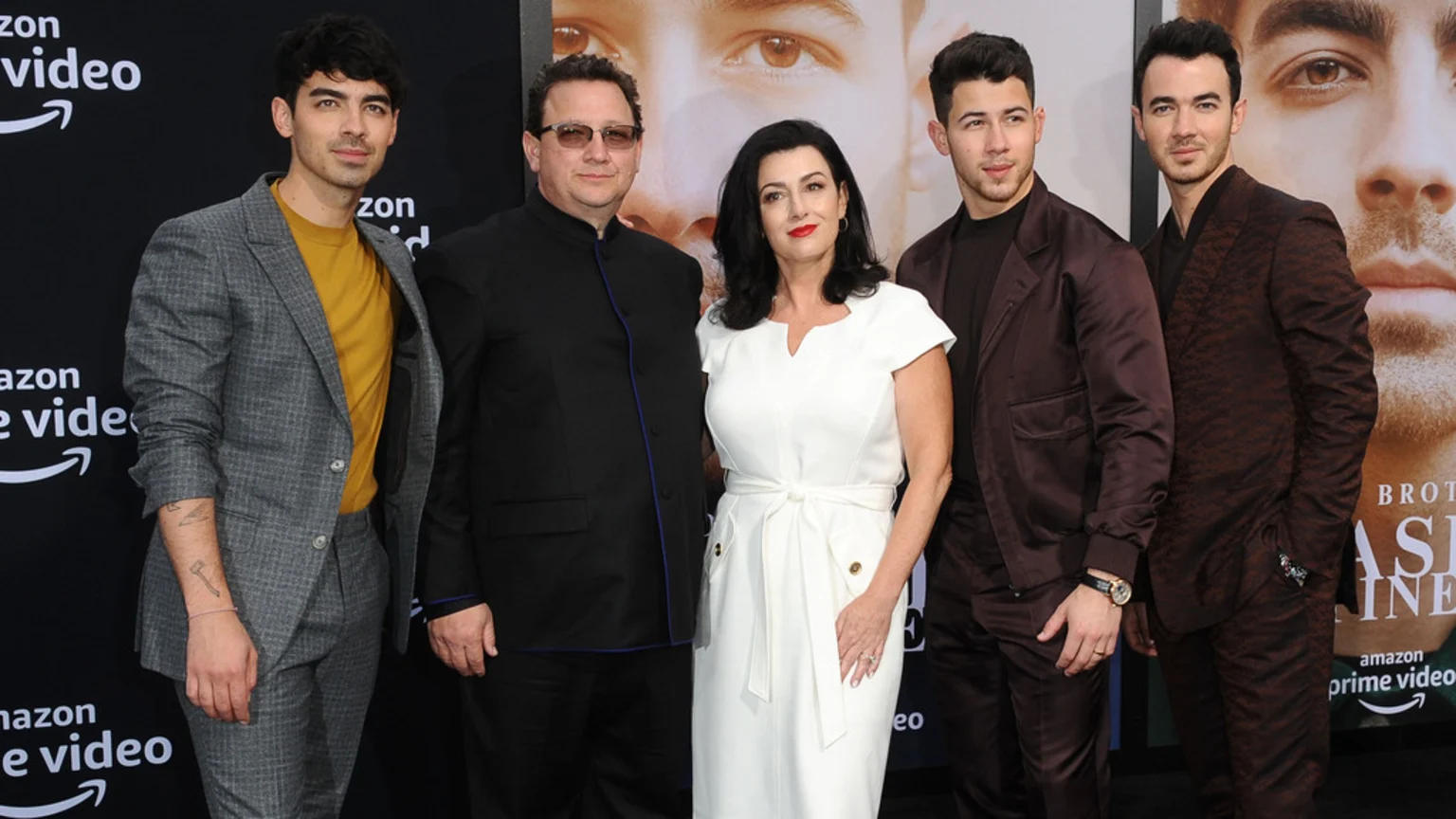 Joe Jonas, an older man, an older woman in a white dress, Nick Jonas, and Kevin Jonas pose at an event with Amazon Prime Video branding in the background.