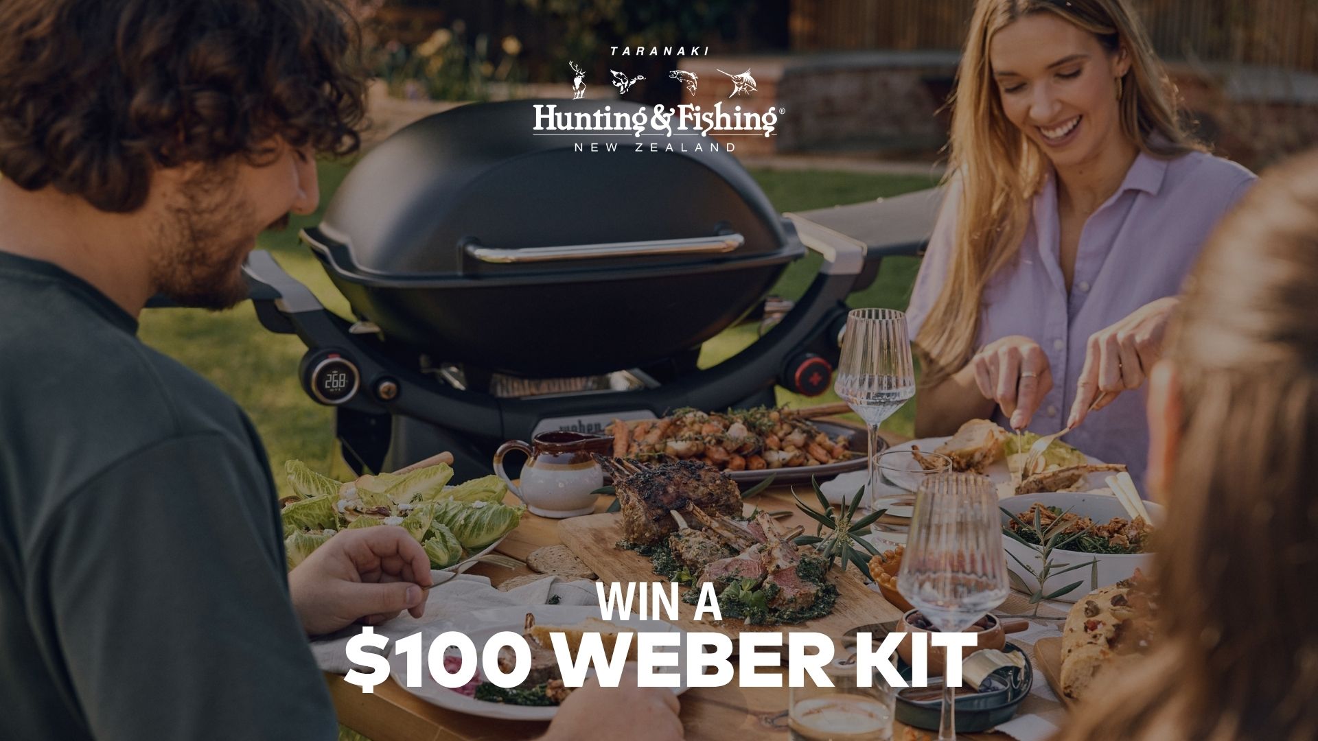 A group of people enjoy an outdoor meal with a prominent black Weber grill in the background, featuring text overlays "WIN A $100 WEBER KIT" and "Hunting & Fishing New Zealand".
