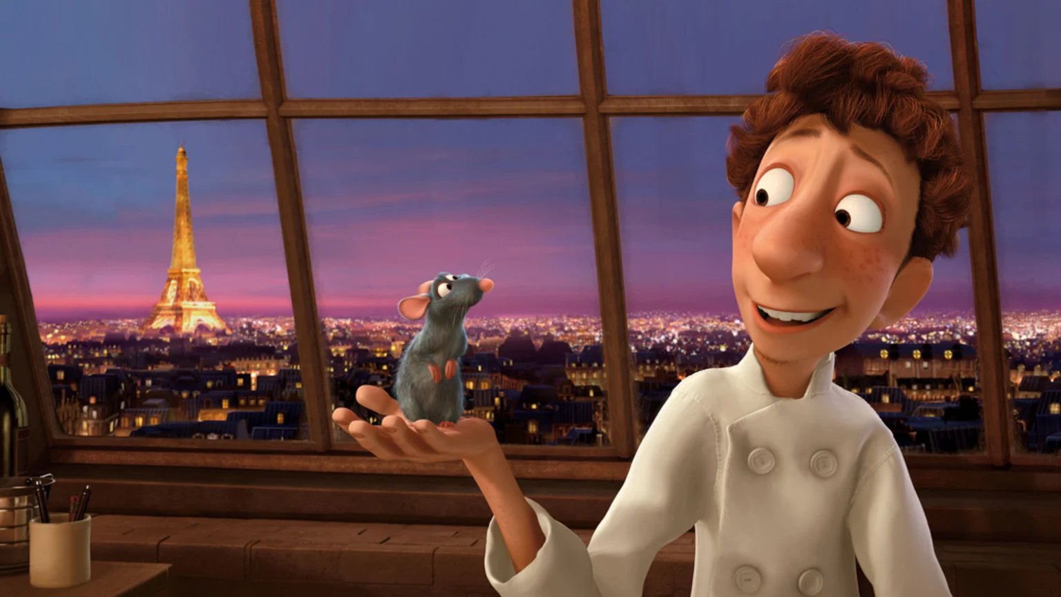 An animated chef in a white jacket holds a small gray rat on his hand, with the illuminated Eiffel Tower and a panoramic view of Paris at dusk visible through a large window.