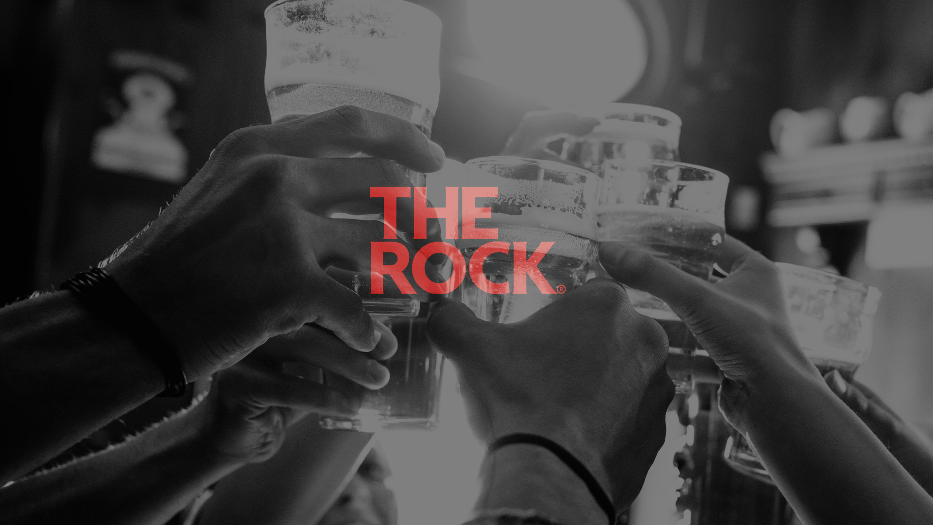 The Rock logo on top of a black and white image of people 'cheers-ing' glasses at a pub