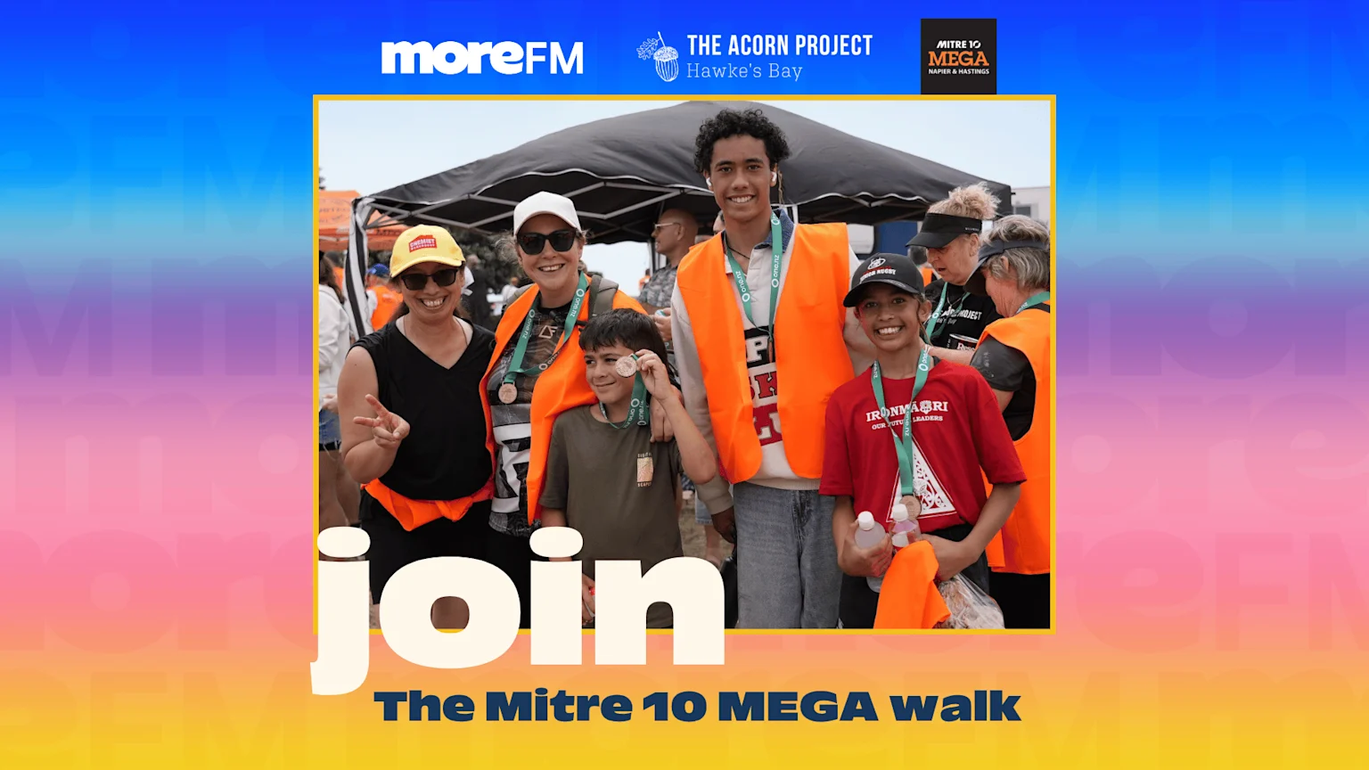 A diverse group of smiling people, including adults and children wearing orange vests and medals, at what appears to be the Mitre 10 MEGA walk event.