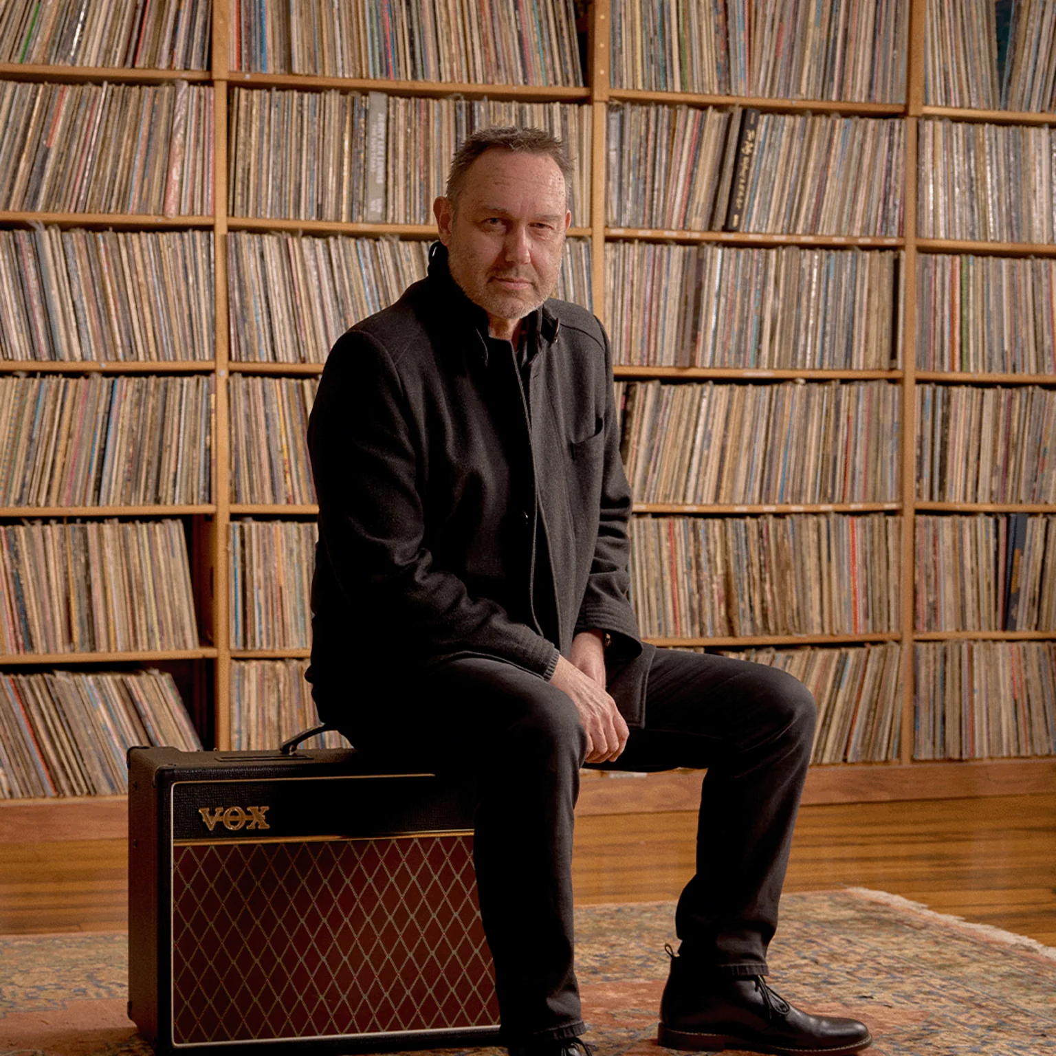 Mark 'Woodsie' Hazelwood sits on VOX amp in front of vinyl record collection wall