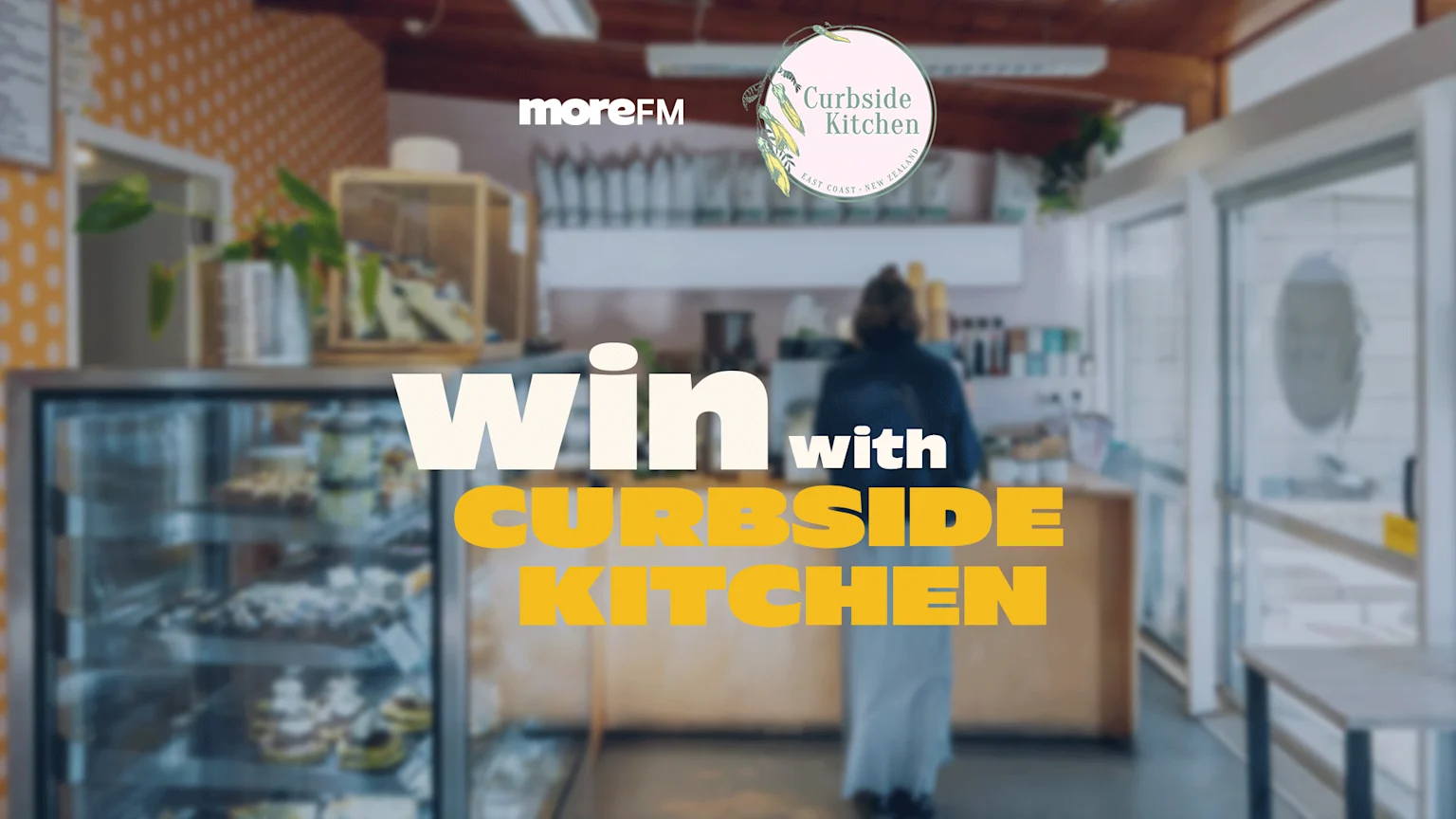 A blurred cafe interior features "Win with Curbside Kitchen" text, a "moreFM" logo, the "Curbside Kitchen East Coast New Zealand" logo, a person, and a display fridge.