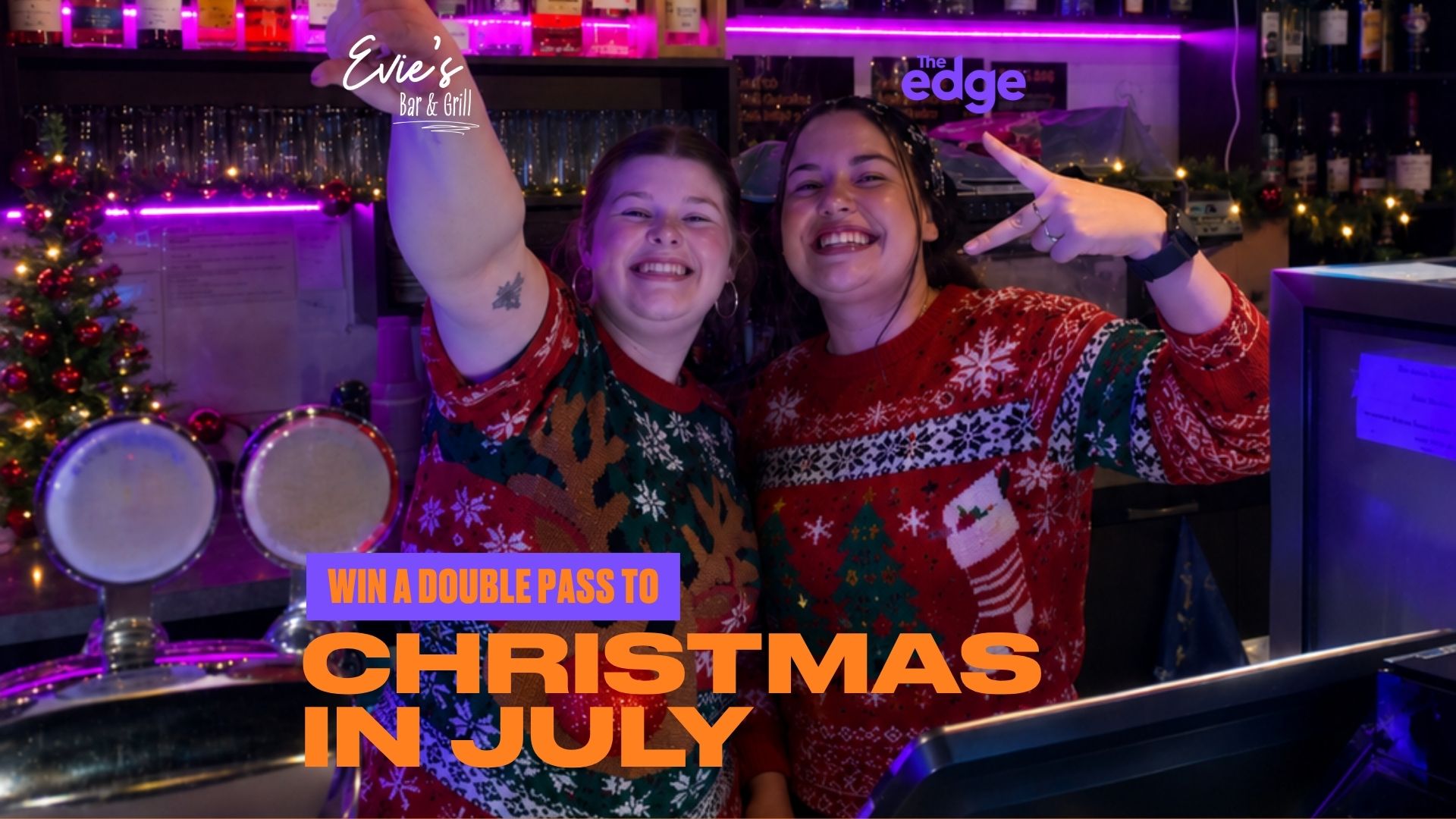 Two smiling women in festive Christmas sweaters pose behind a decorated bar with an "Evie's Bar & Grill" sign, and text "WIN A DOUBLE PASS TO CHRISTMAS IN JULY".