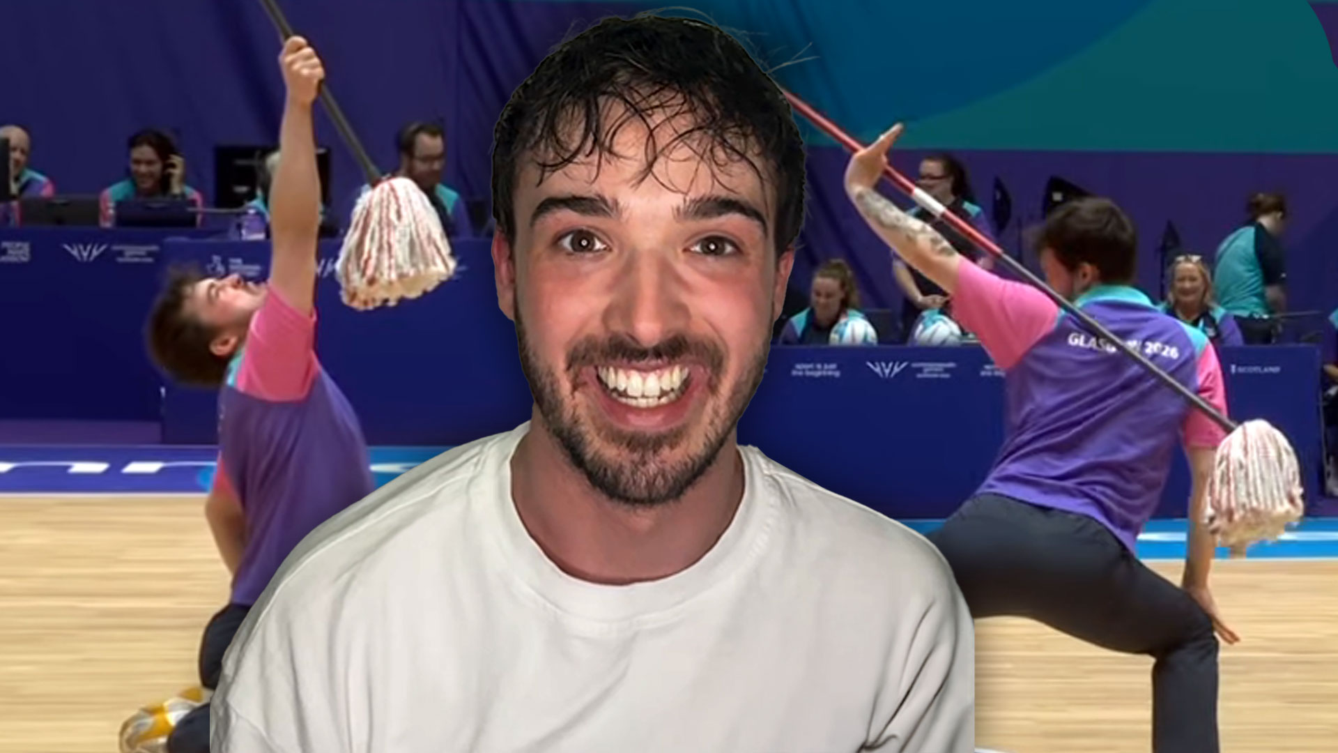 A smiling man with a beard is in the foreground, superimposed over a background scene of two people in purple and pink shirts performing with mops on a court, one kneeling and one squatting.