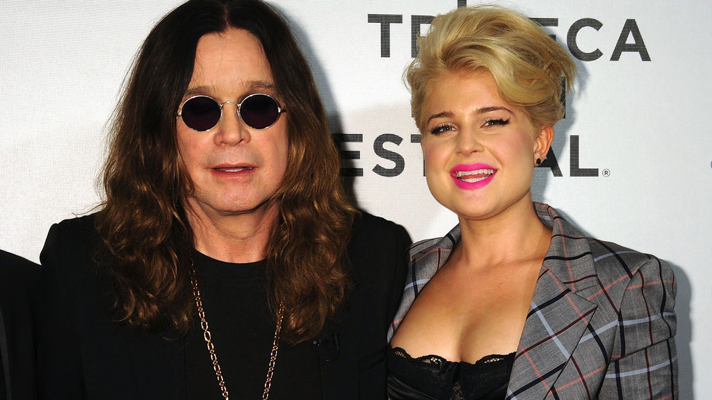 Ozzy Osbourne, in sunglasses and a black shirt, poses beside his daughter Kelly Osbourne, with blonde hair, bright pink lipstick, and a plaid blazer, at a Tribeca Festival event.