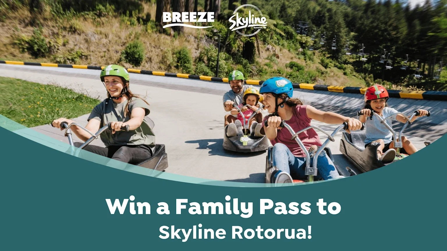 A smiling family of four, including two adults and two children in helmets, rides luge carts down a track at Skyline Rotorua on a sunny day.