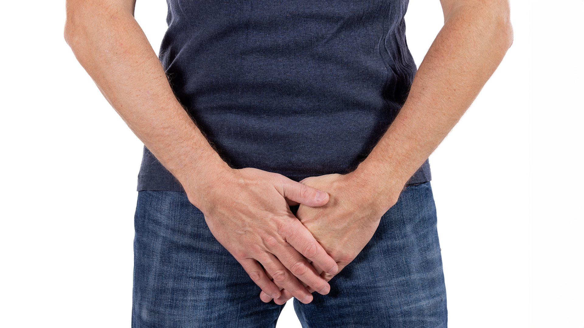 A man standing with pants on, with his hands hovering over his penis