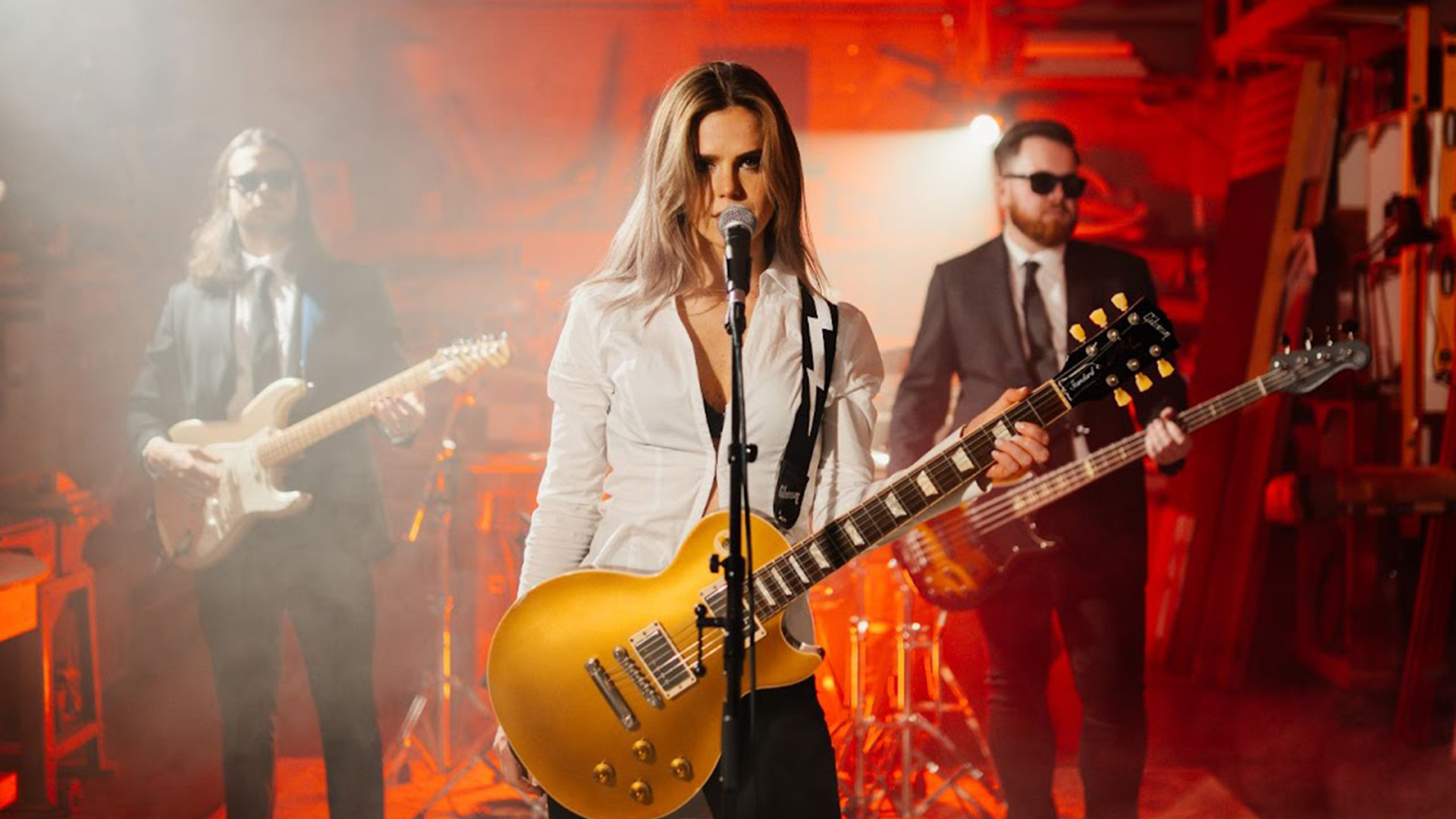 Cassie holding a guitar with two omre guitarists in the background