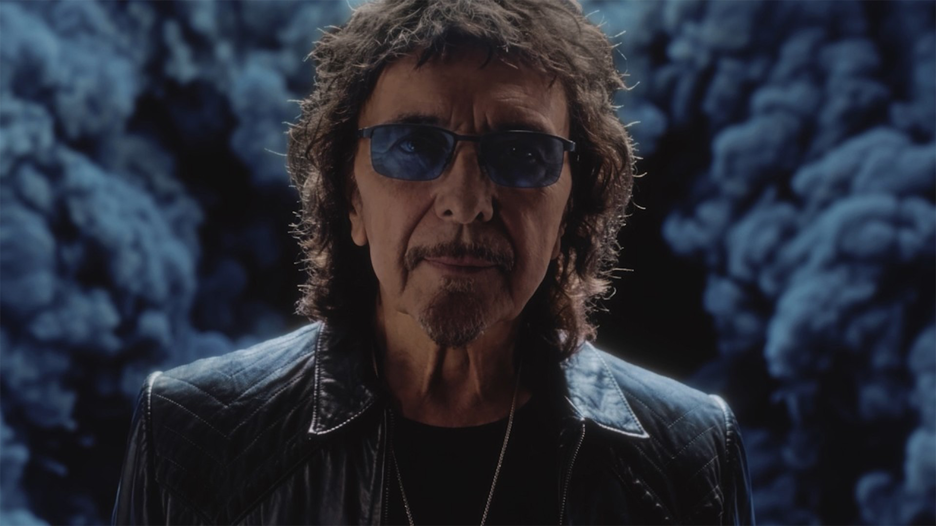 Tony Iommi looking at the camera, dark smoke behind him