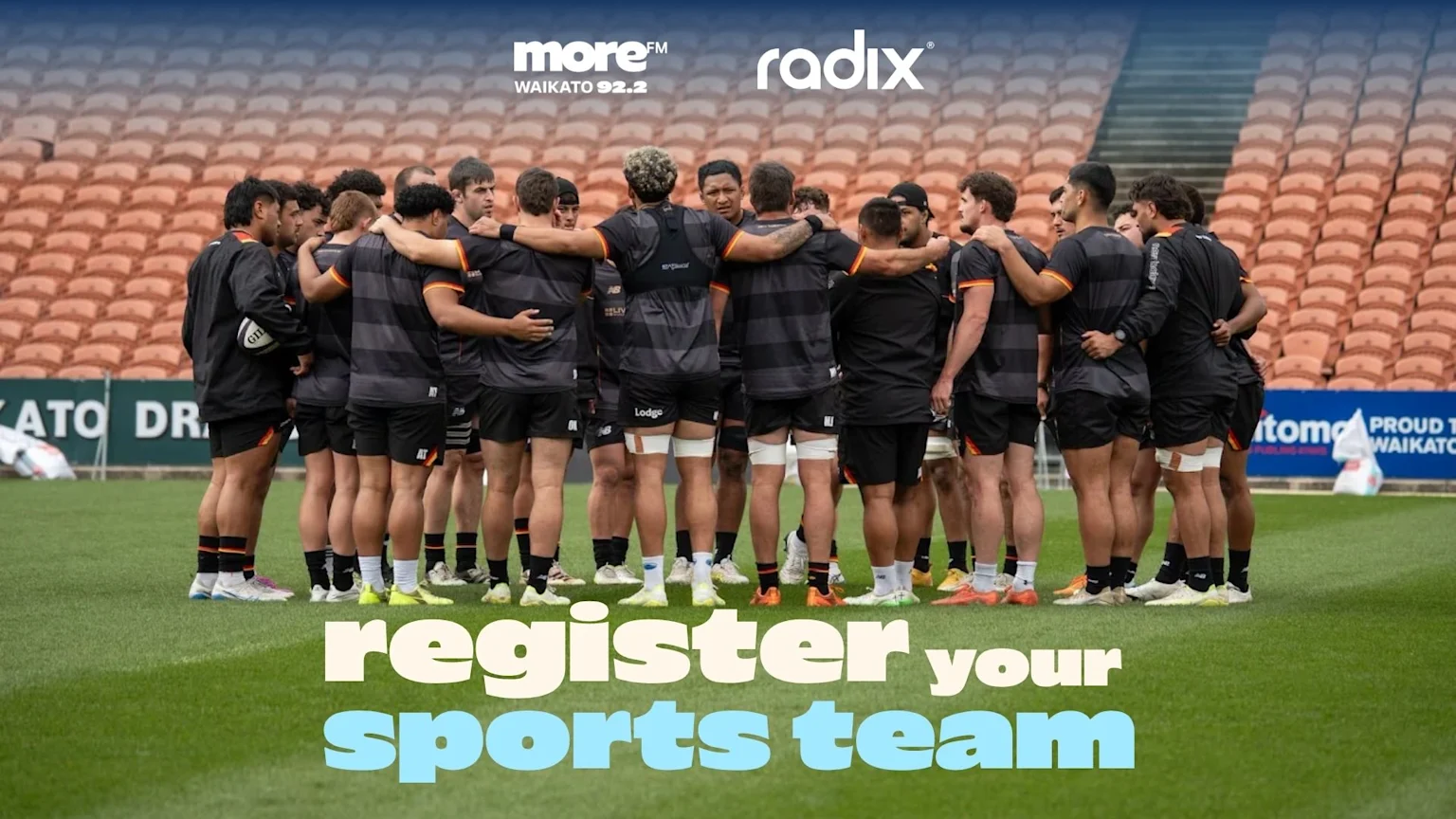 A group of rugby players in black and orange uniforms huddle on a field with a stadium in the background, beneath "moreFM" and "radix" logos, and text saying "register your sports team".