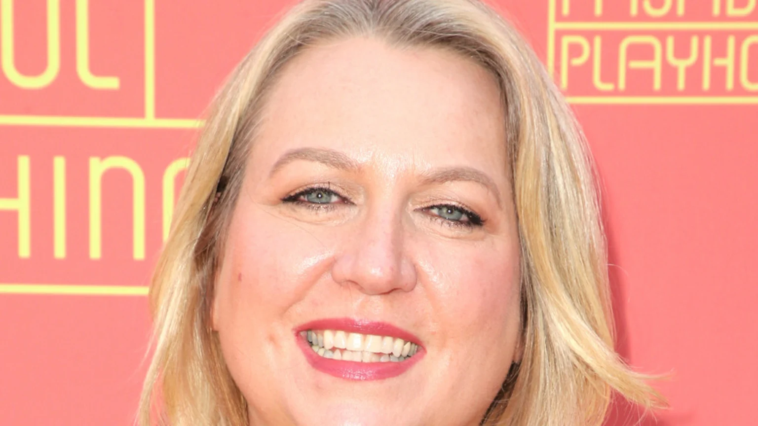 A close-up headshot shows a smiling woman with blonde hair and blue eyes looking at the camera, against a red background with yellow text.