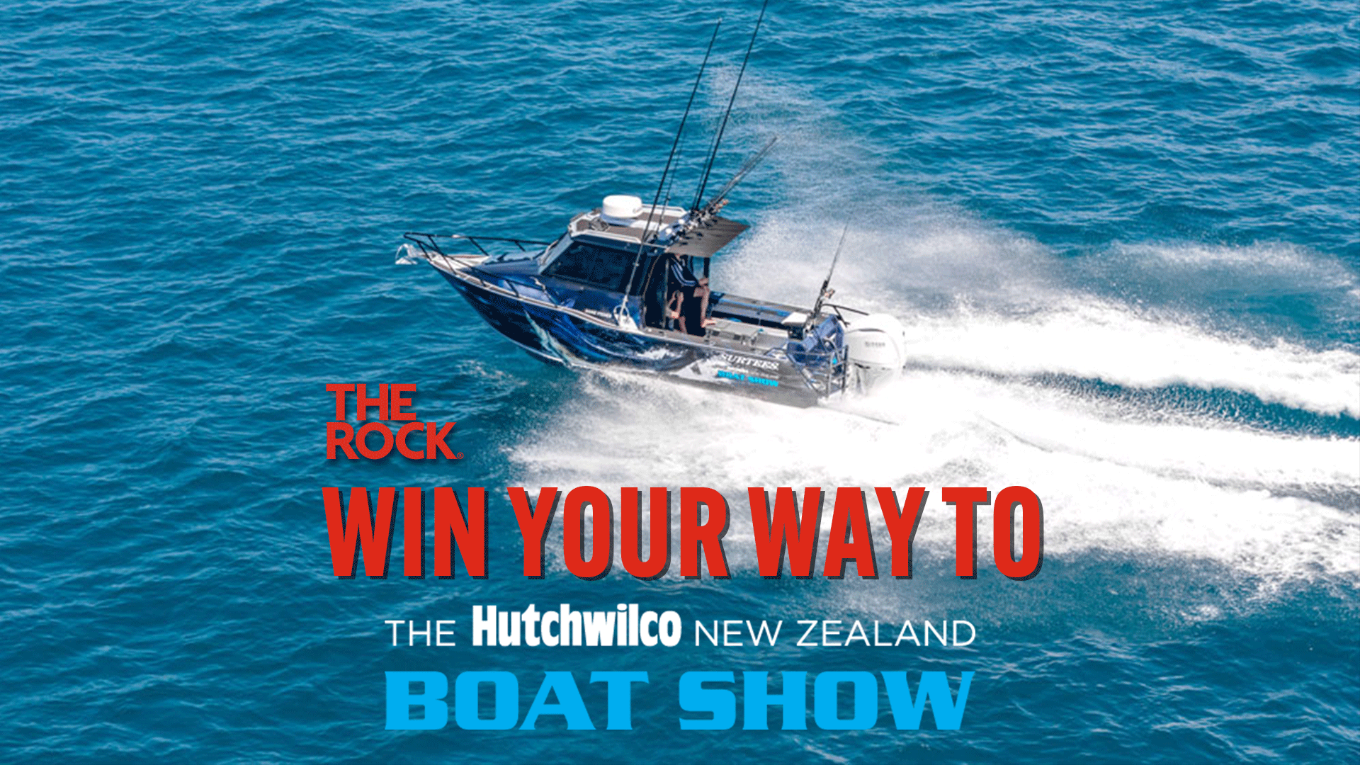 A blue fishing boat with multiple rods speeds on a blue ocean, creating a white wake, with text "THE ROCK WIN YOUR WAY TO THE Hutchwilco NEW ZEALAND BOAT SHOW" overlaid.