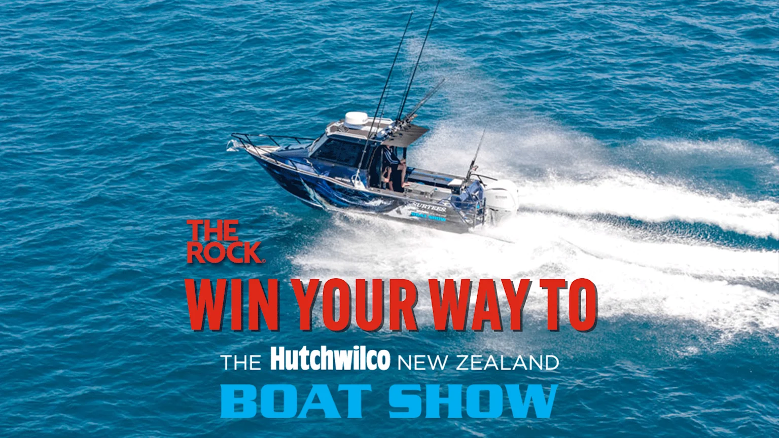 A blue fishing boat with multiple rods speeds on a blue ocean, creating a white wake, with text "THE ROCK WIN YOUR WAY TO THE Hutchwilco NEW ZEALAND BOAT SHOW" overlaid.