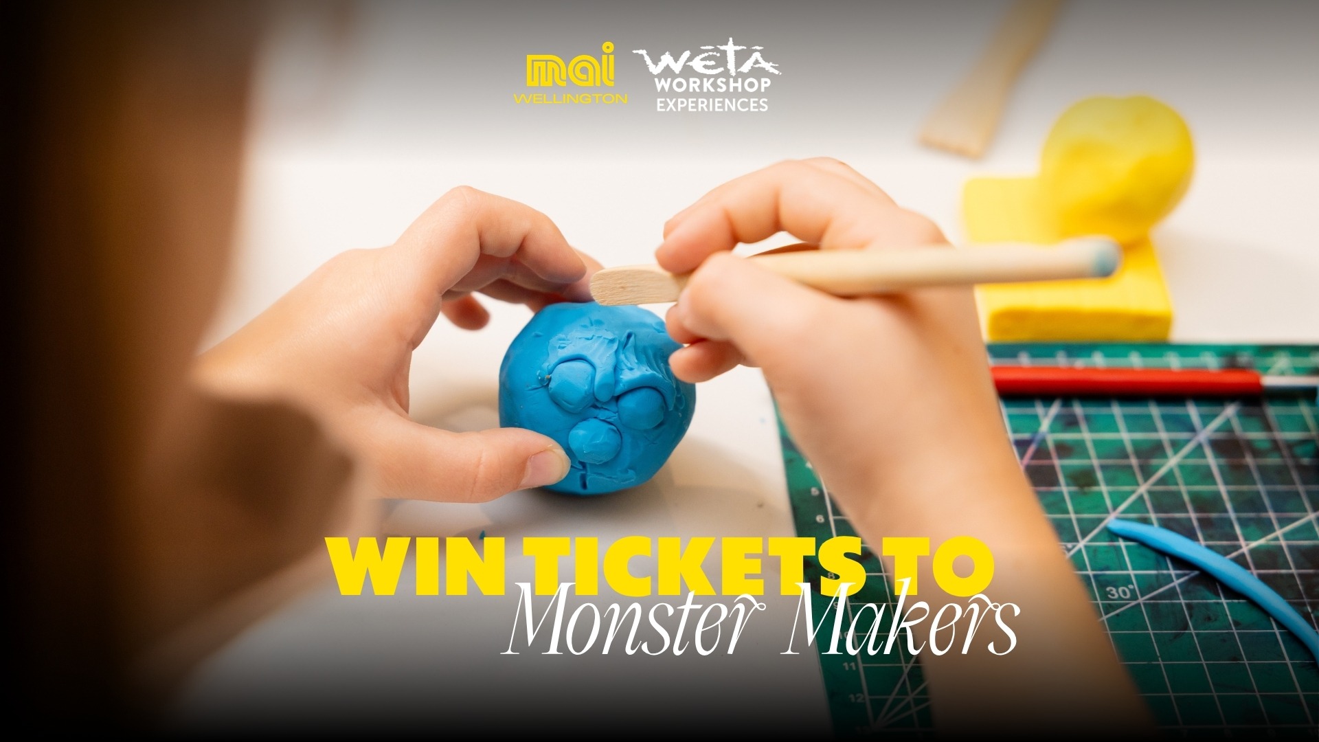 A child's hands use a sculpting tool to shape a blue clay monster face, with a green cutting mat, yellow clay, "mai WELLINGTON" and "WĒTĀ WORKSHOP EXPERIENCES" logos, and "WIN TICKETS TO Monster Makers" text.