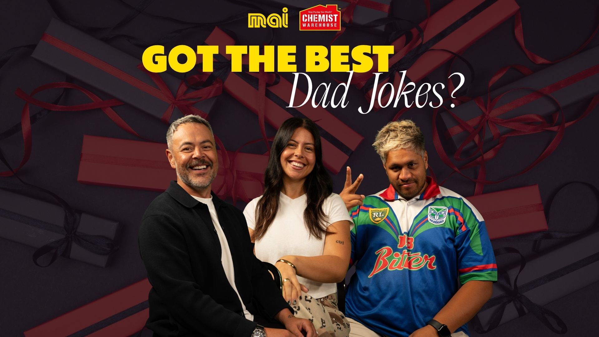 Three smiling people, two men and one woman, are in the foreground with blurred gift boxes in the background, and text reading "GOT THE BEST Dad Jokes?" along with Mai and Chemist Warehouse logos.