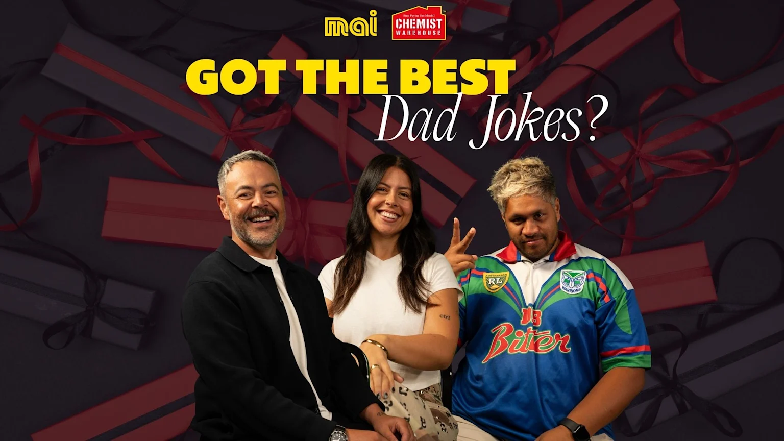Three smiling people, two men and one woman, are in the foreground with blurred gift boxes in the background, and text reading "GOT THE BEST Dad Jokes?" along with Mai and Chemist Warehouse logos.