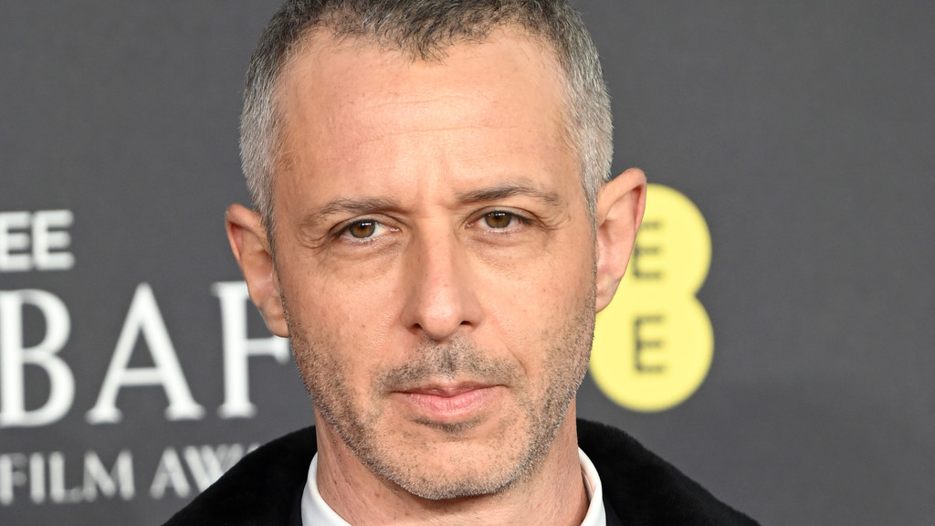 Actor Jeremy Strong looks directly at the camera, sporting short graying hair and light stubble, against a dark background with the partial BAFTA logo.