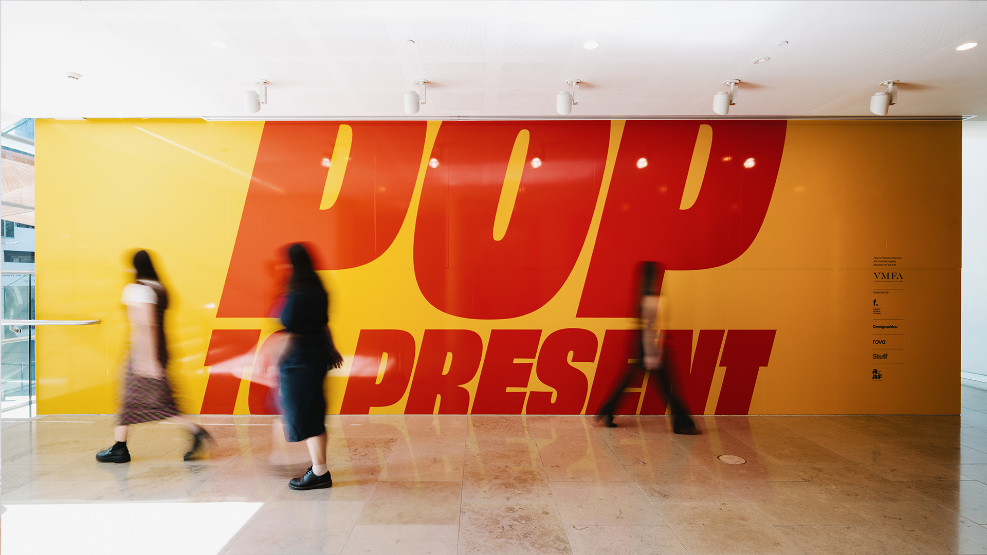 People walking past bright POP to PRESENT wall