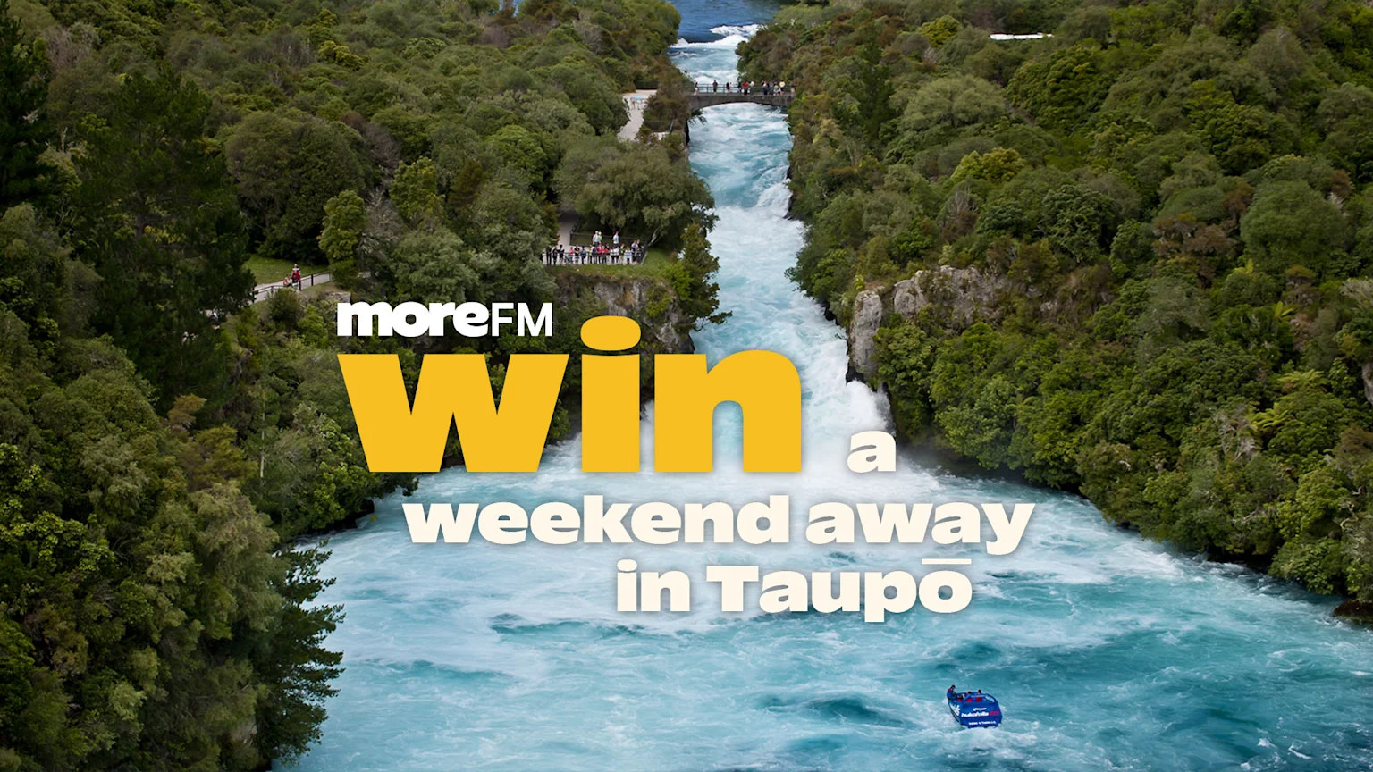 A river with rapids winds through a dense green forest, featuring a bridge, people, and a jet boat, with text: "moreFM Win a weekend away in Taupō".