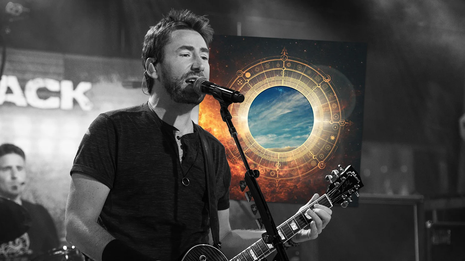A black and white image shows a male musician singing into a microphone and playing an electric guitar, with a vibrant celestial wheel poster featuring a blue sky in the background.