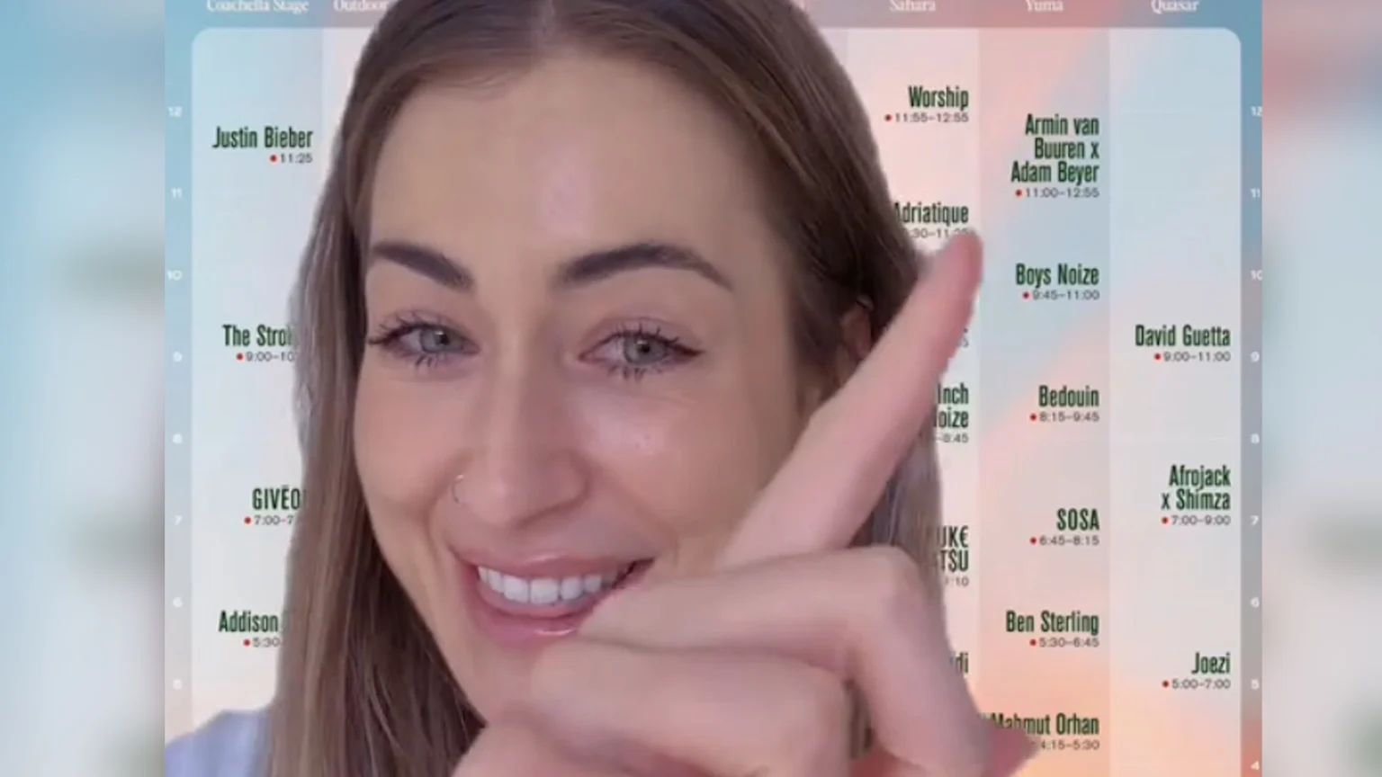 A smiling woman with a nose ring points with her right index finger at a Coachella set time schedule behind her, listing artists such as Justin Bieber, Worship, Armin van Buuren, and David Guetta.
