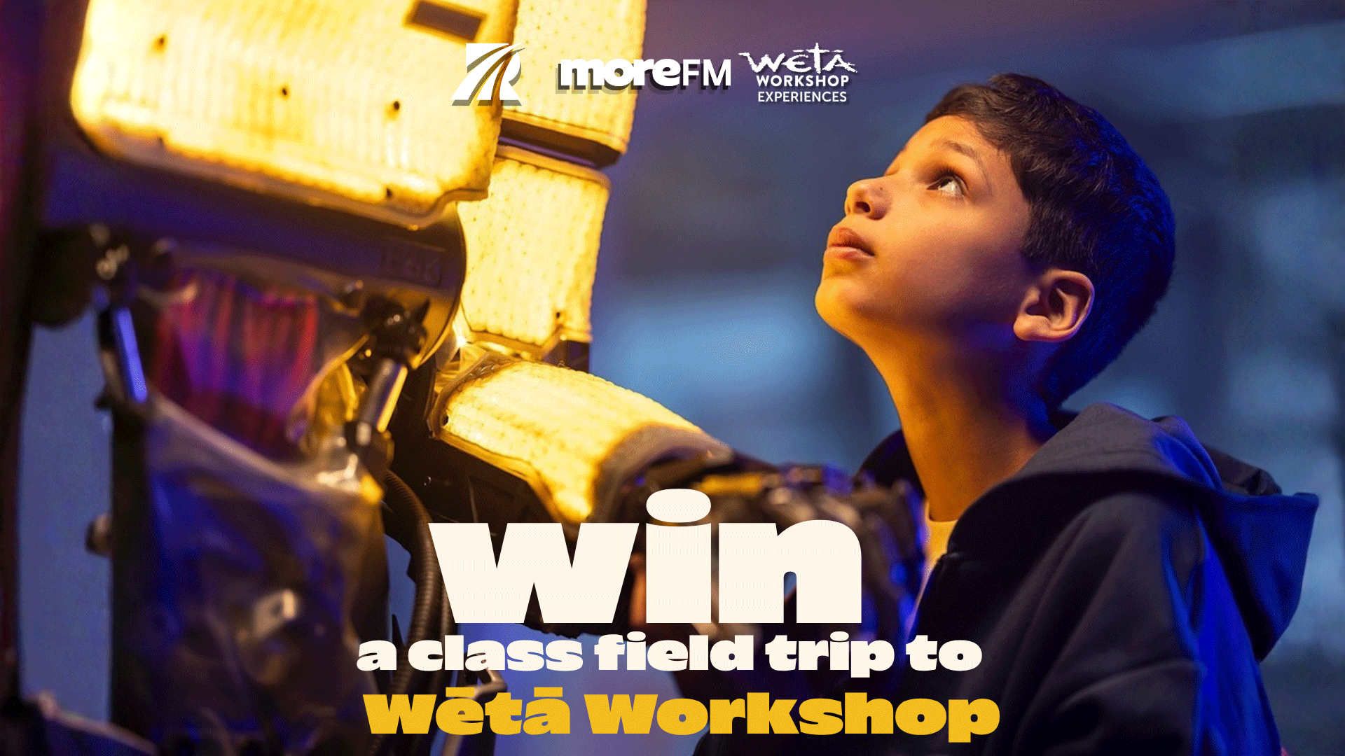 A young boy looks up in wonder at a large, glowing yellow object, with prominent text that reads "Win a class field trip to Wētā Workshop" and logos for MoreFM and Wētā Workshop.