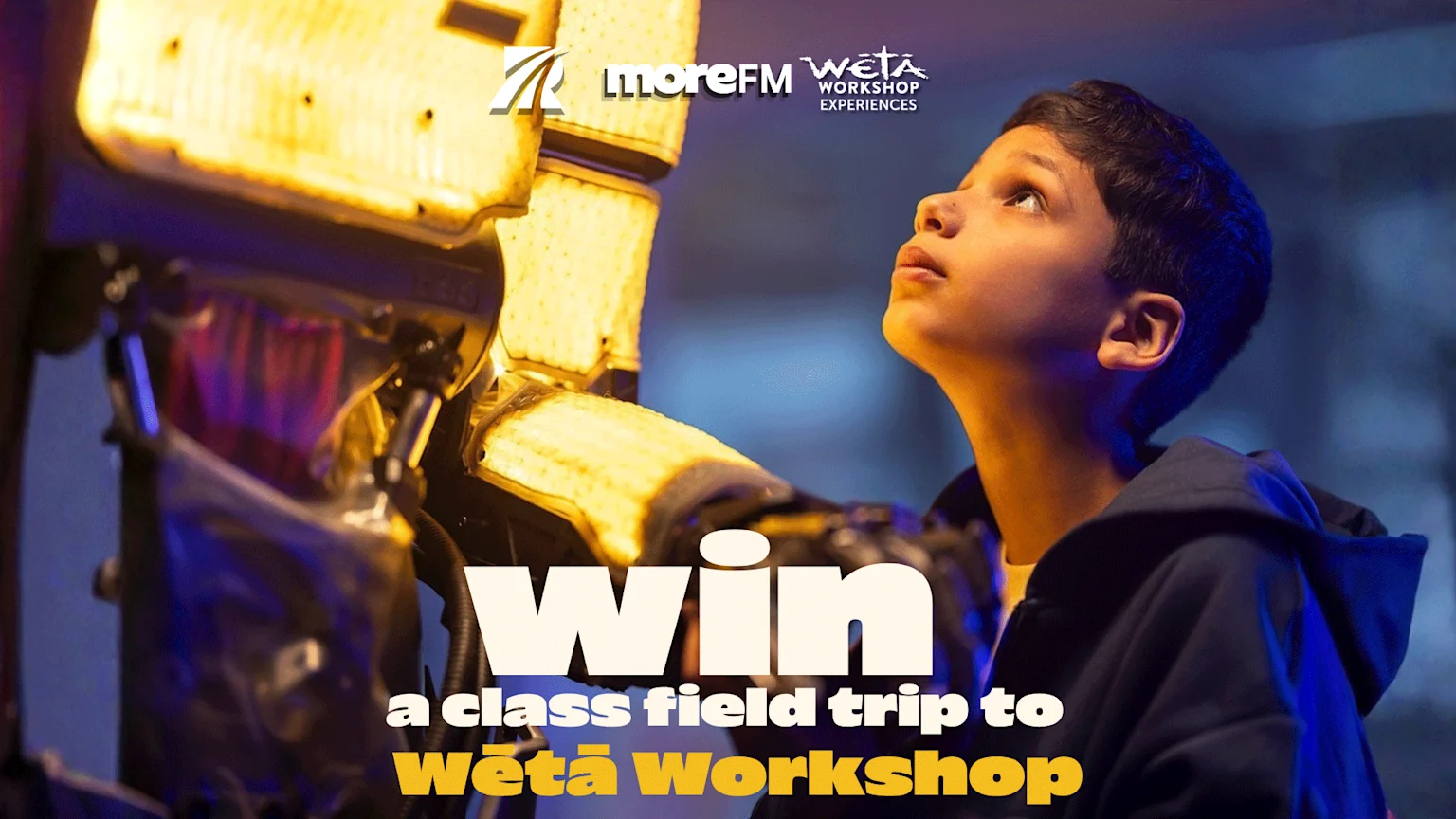 A young boy looks up in wonder at a large, glowing yellow object, with prominent text that reads "Win a class field trip to Wētā Workshop" and logos for MoreFM and Wētā Workshop.