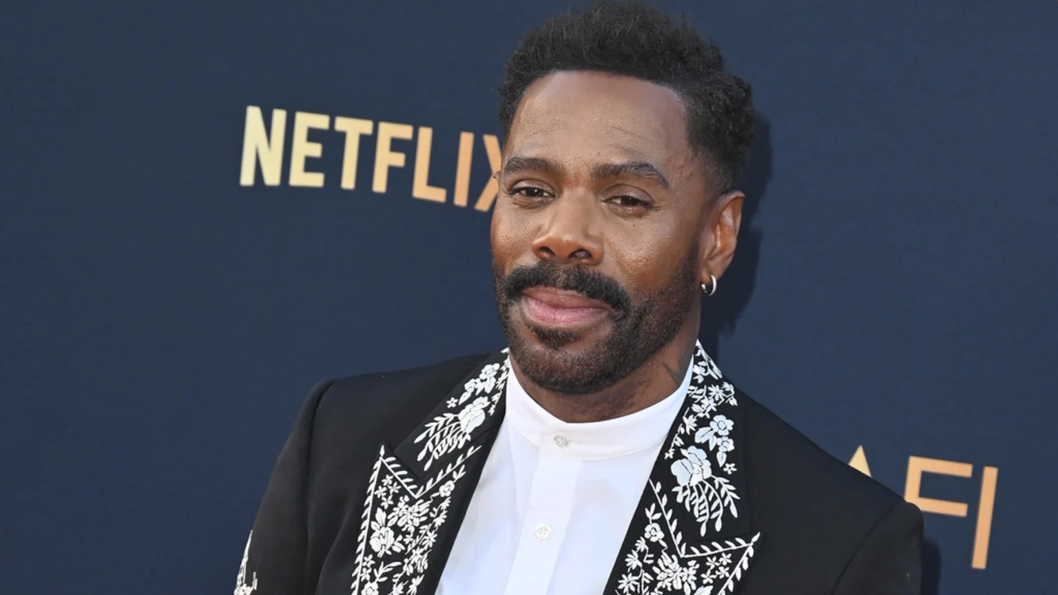 Colman Domingo smiles, wearing a black suit with white floral embroidery and a white shirt, against a dark background with "NETFLIX" and "AFI" logos.
