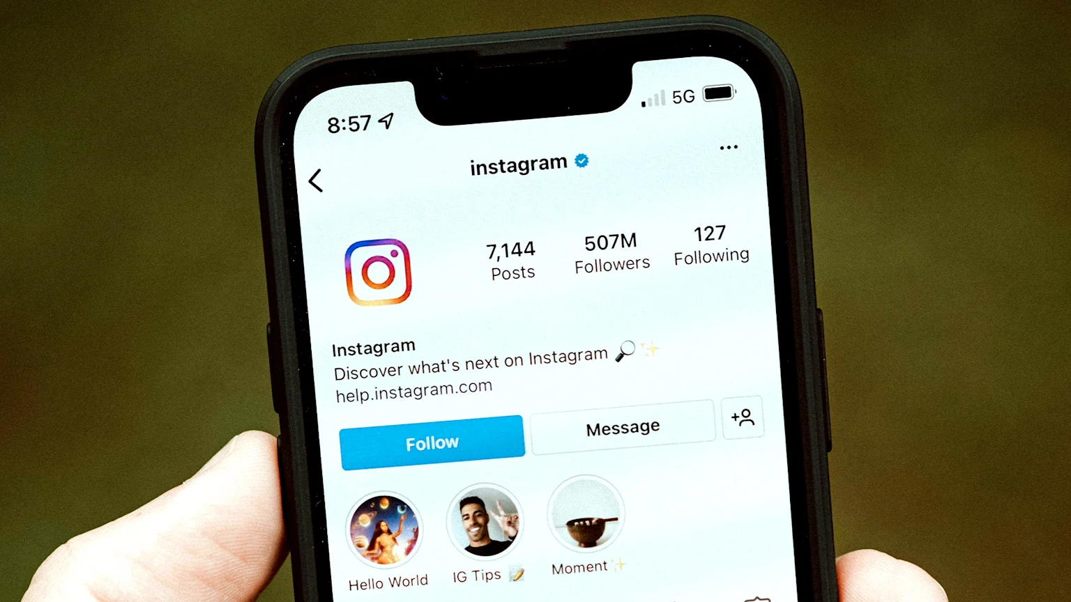 A close-up of an iPhone screen displays the official Instagram app profile, showing "instagram" with 507M followers, 7,144 posts, and a visible "Follow" button.